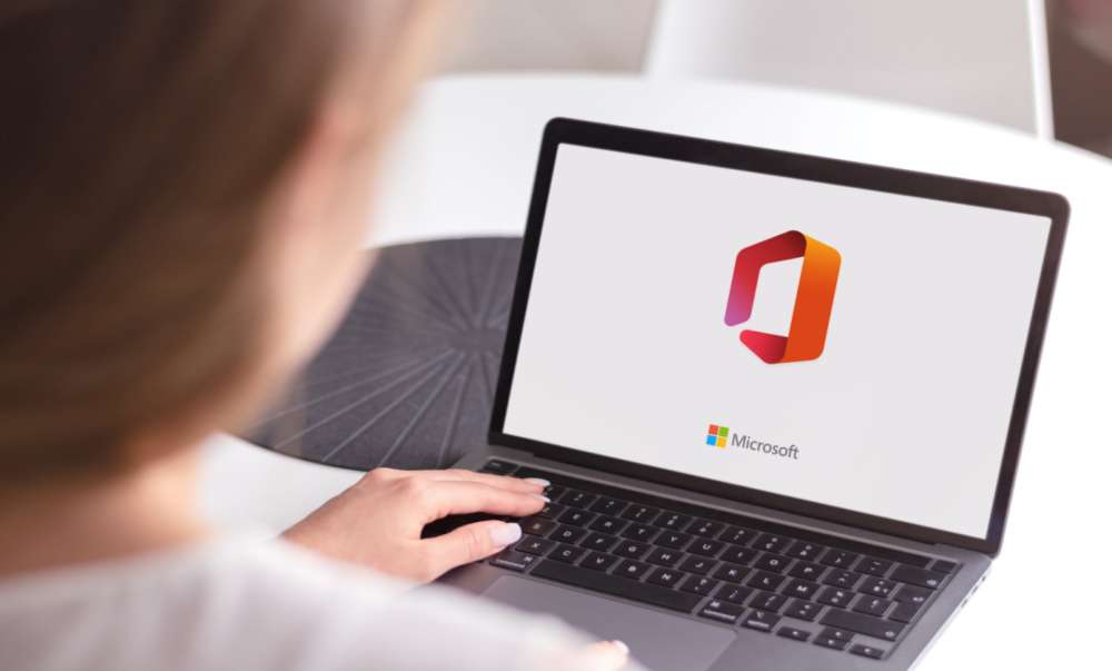 Person using a laptop displaying the Microsoft Office logo, representing Microsoft 365 software, cloud productivity tools, and modern business technology.