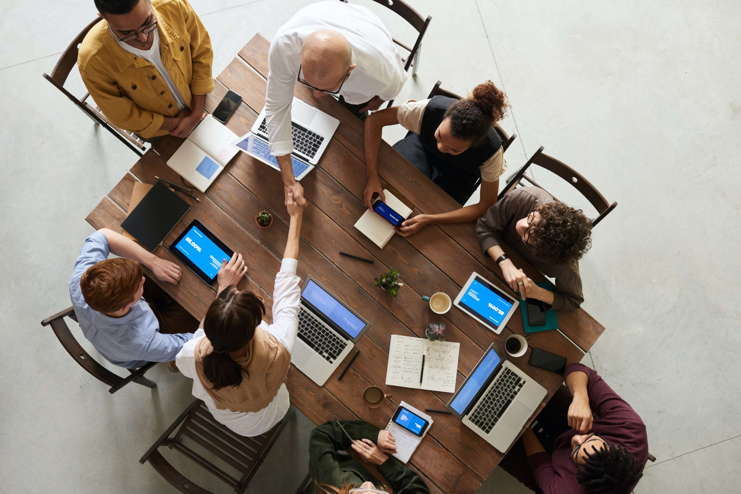 Overhead view of a diverse team collaborating around a conference table with laptops, tablets, and notebooks, showing teamwork, strategy planning, and modern office collaboration.