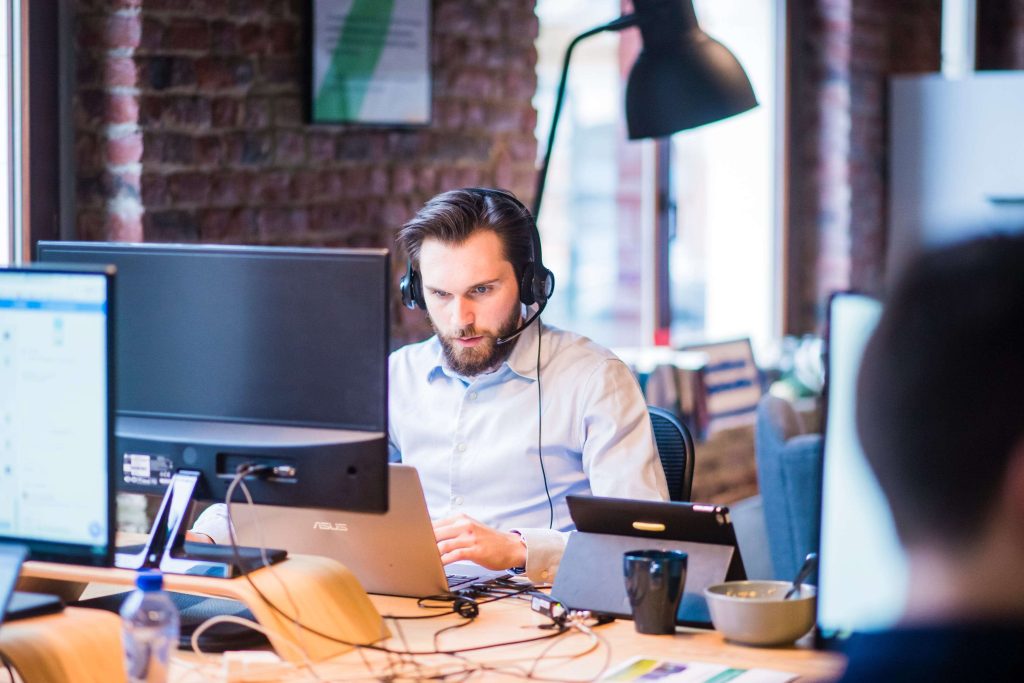 IT professional wearing a headset working at a desk with multiple monitors and a laptop in a modern office, representing technical support, remote troubleshooting, and workplace productivity.