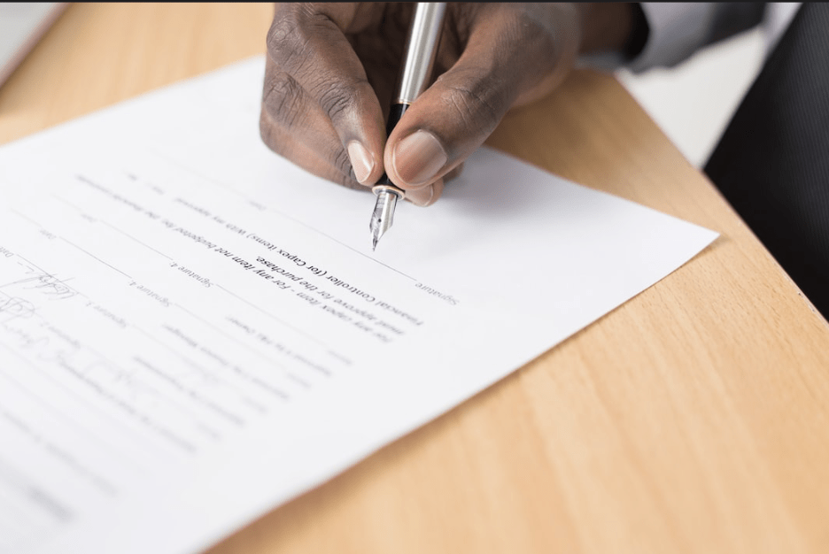 Close-up of a person signing a business document with a pen on a wooden desk, representing contracts, agreements, or professional paperwork