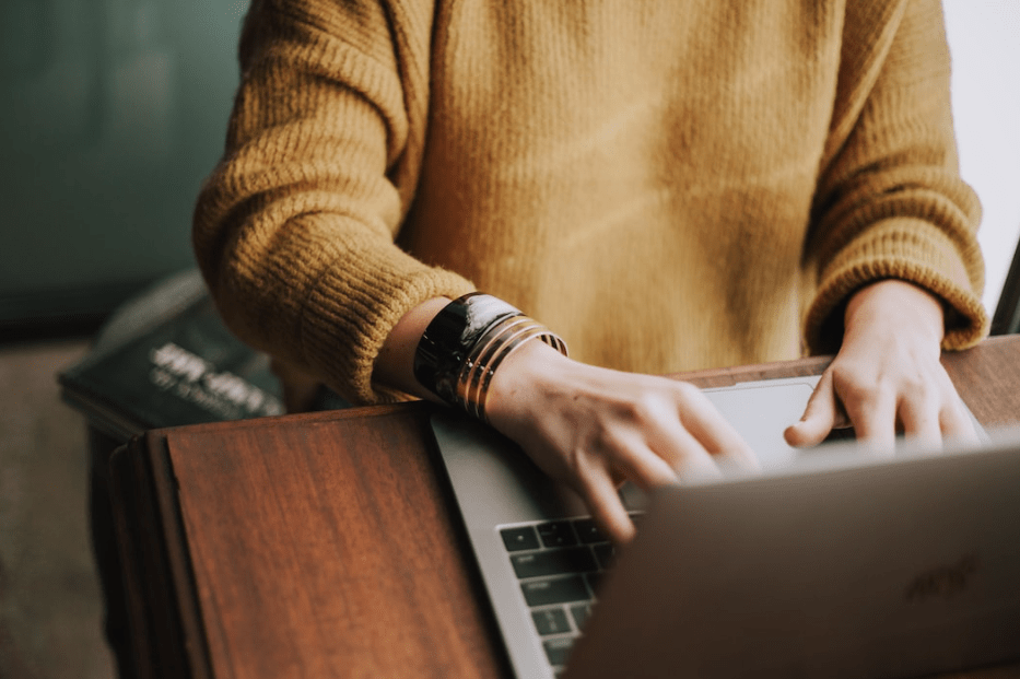 Person typing on a laptop at a wooden desk, representing remote work, content creation, or digital productivity