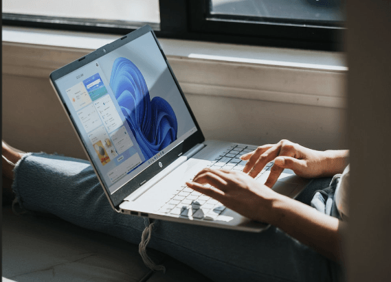Person using a laptop running Windows 11 while sitting near a window, representing modern remote work and productivity