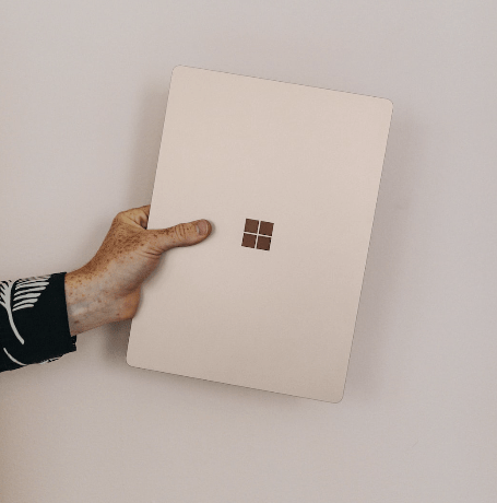 Hand holding a closed Microsoft Surface laptop against a neutral background, showcasing a minimalist modern device design