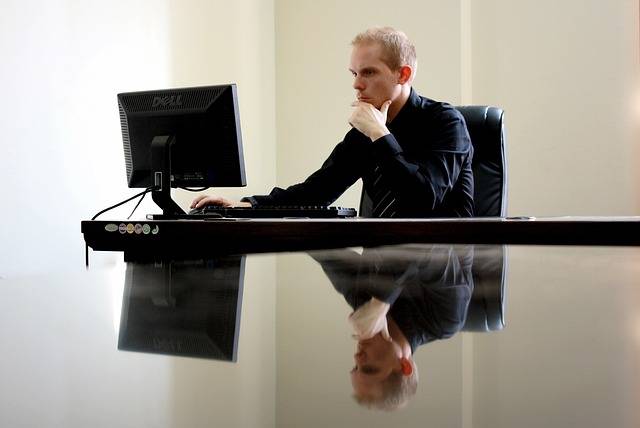 Business professional sitting at a modern desk working on a desktop computer in a minimalist office setting