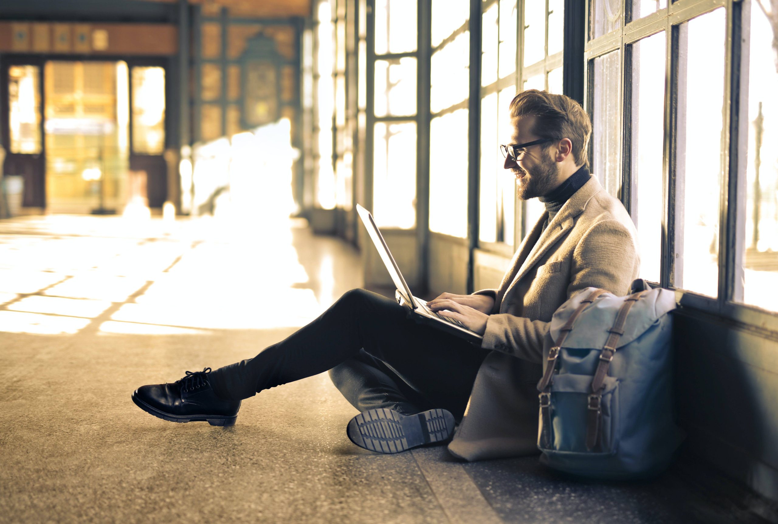 Man sitting on the floor using a laptop in a sunlit hallway