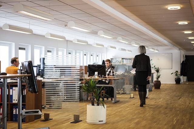 Modern open-plan office with employees working at desks and a manager walking through the workspace