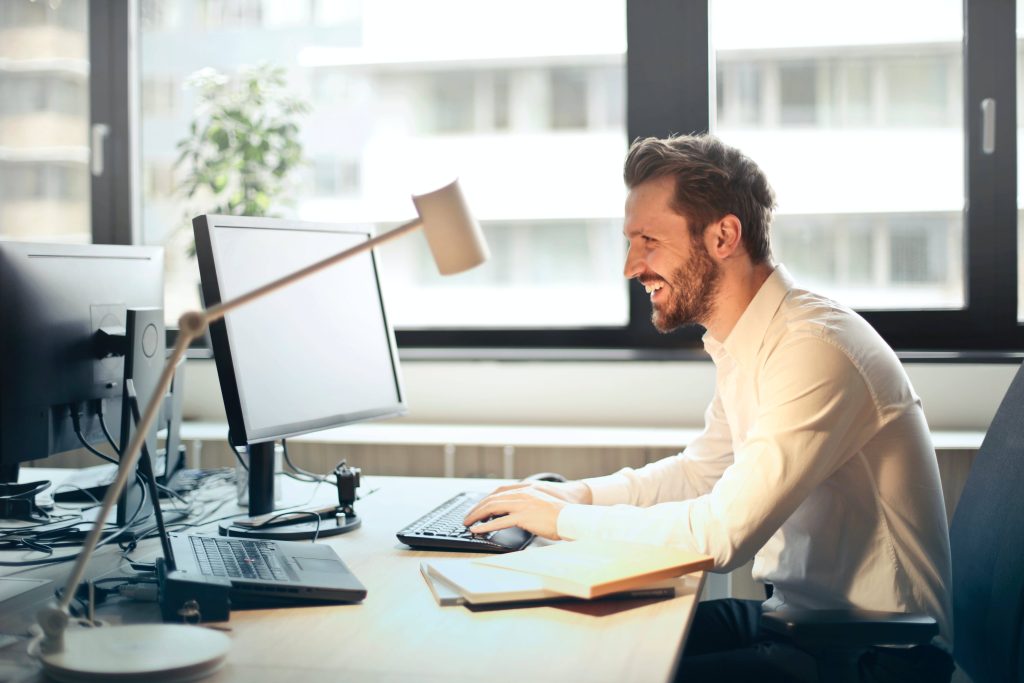 Man smiling while working at a desk with a computer in a bright office