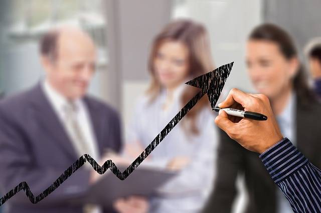Hand drawing an upward trending arrow over a blurred group of business professionals reviewing documents