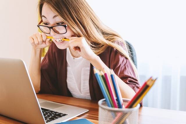 Woman working on a laptop while biting a pencil, showing concentration and problem-solving