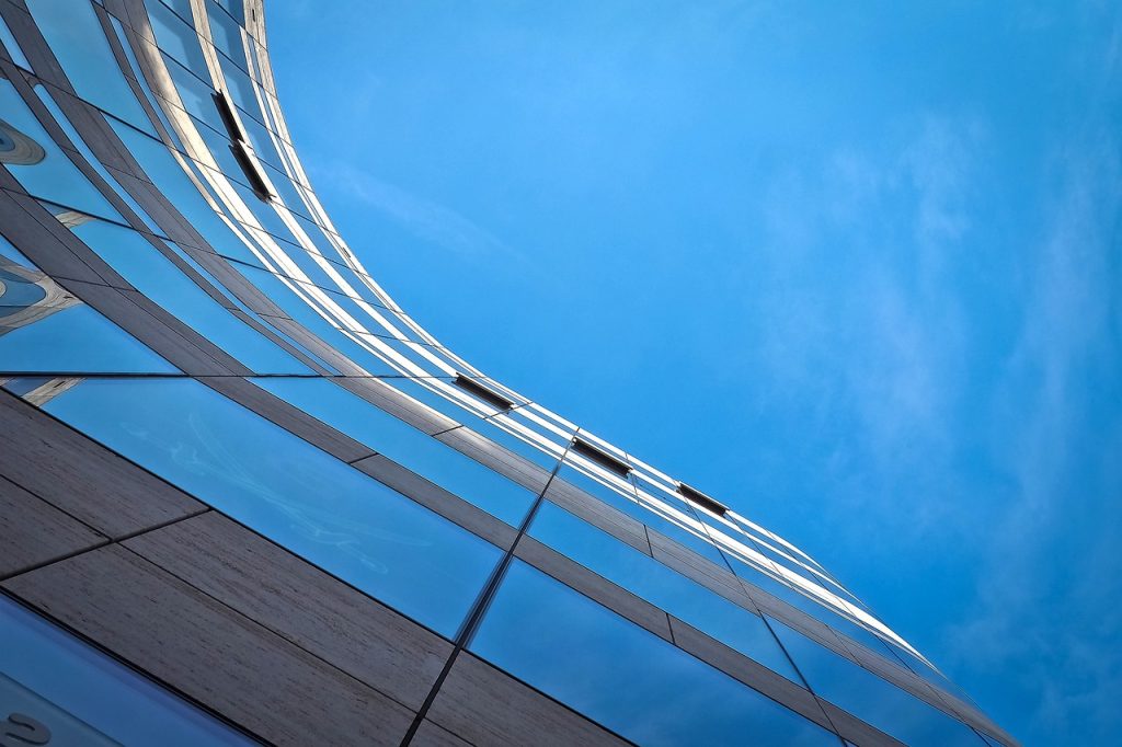 Curved glass office building reflecting a blue sky