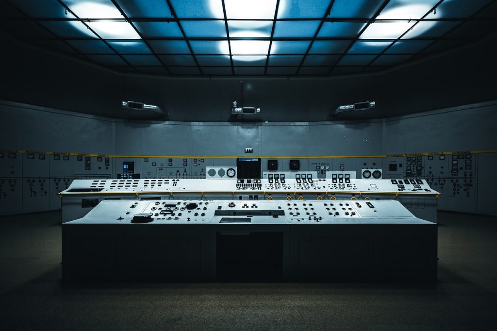Empty industrial control room with large control panels, switches, and monitoring equipment.