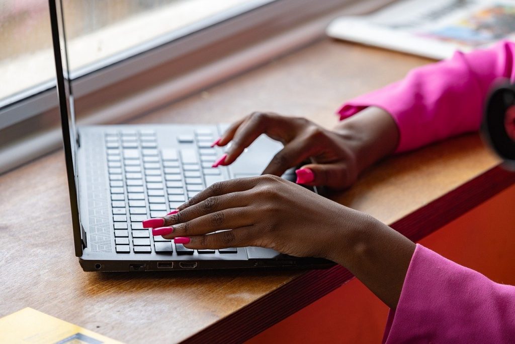 Hands typing on a laptop keyboard at a wooden desk near a window.
