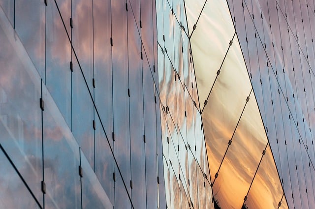 Glass building facade reflecting the sky and clouds at sunset.