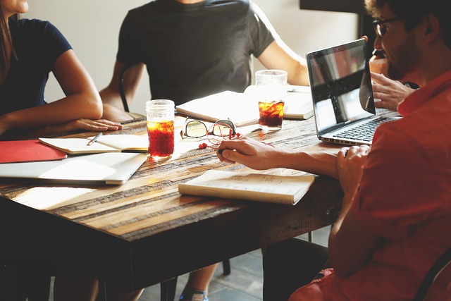Small group seated around a table collaborating with notebooks, laptops, and drinks.