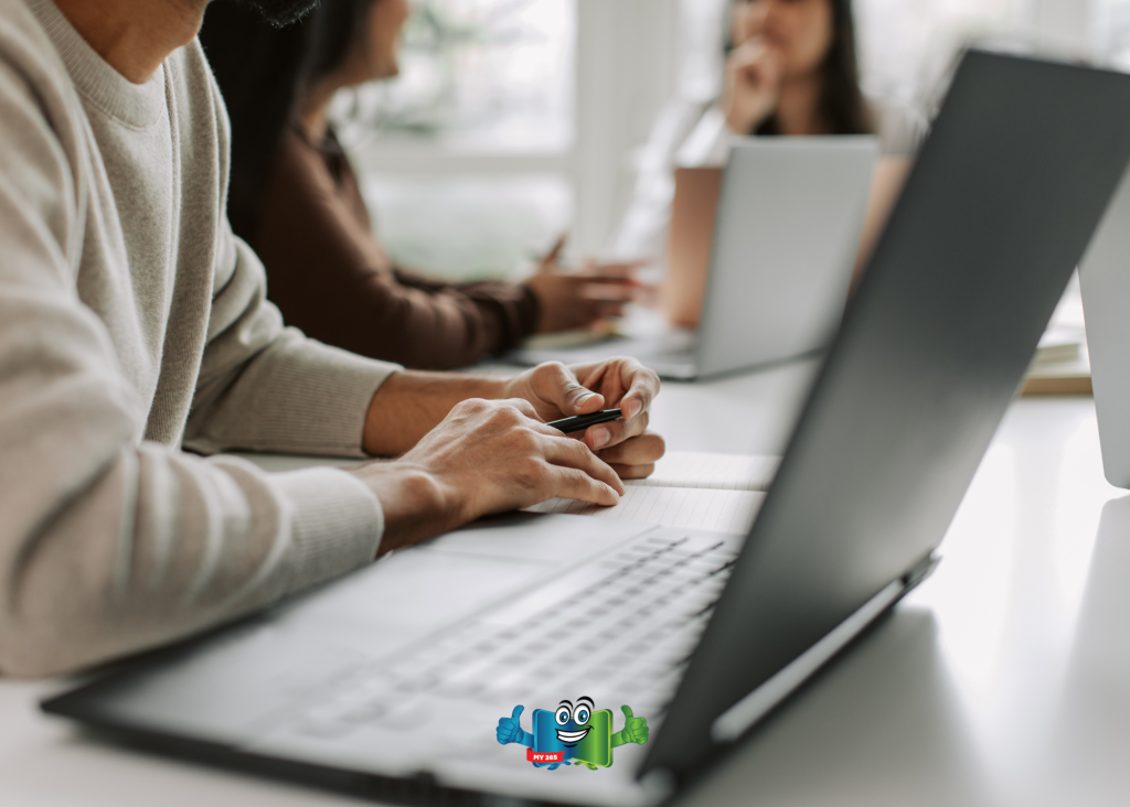 Person working at a laptop while others collaborate in the background.