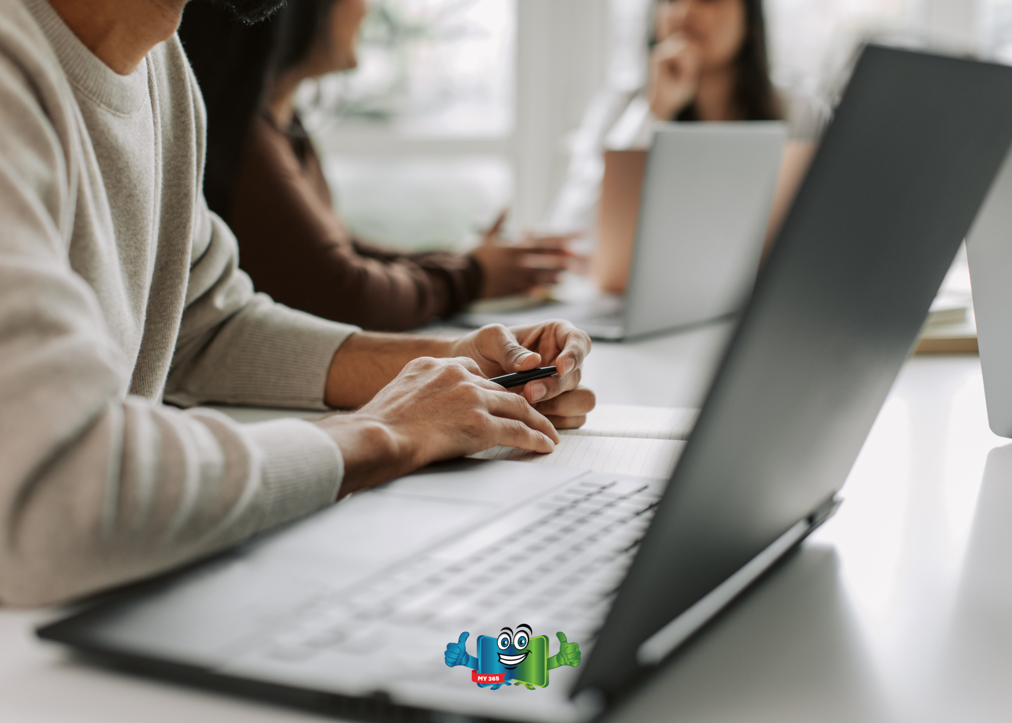 Person working at a laptop while others collaborate in the background.