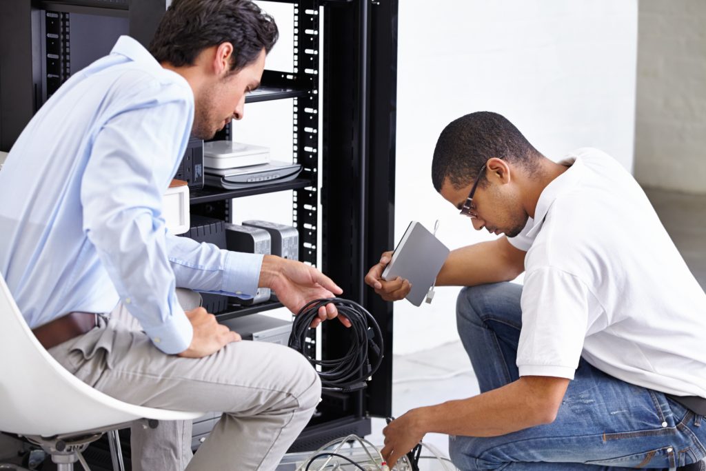 Two IT professionals working on network hardware inside a server rack.