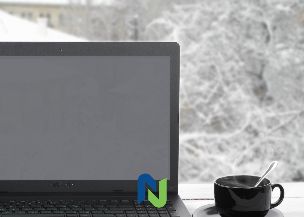 Laptop on a desk beside a steaming coffee with a snowy background.